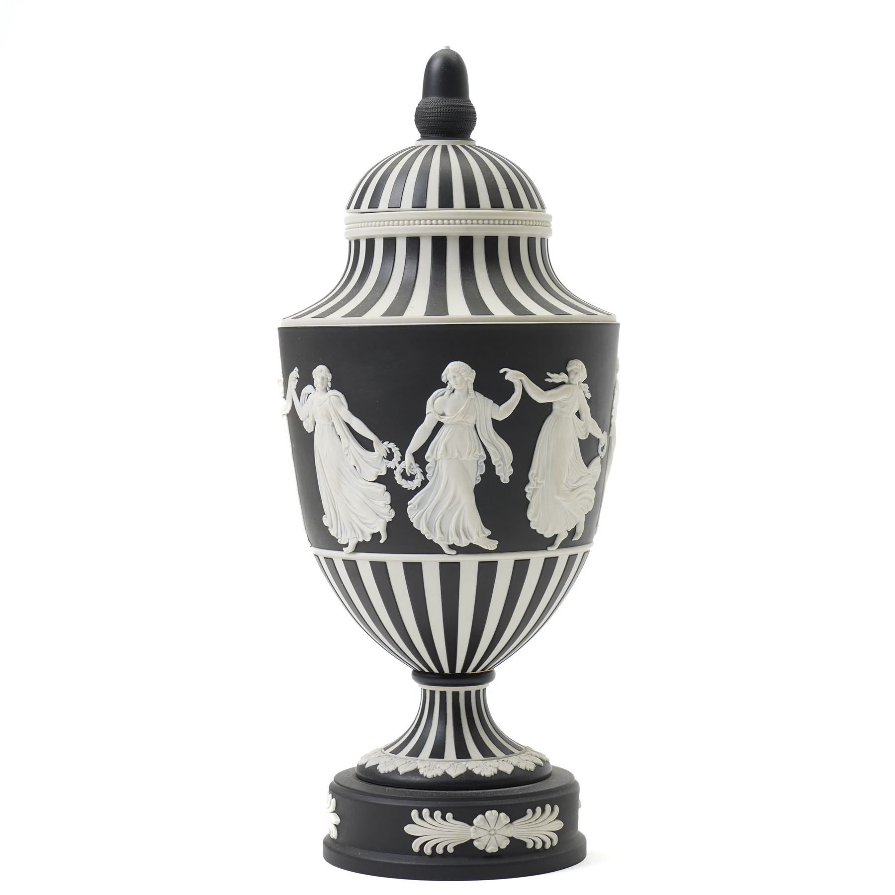 Wedgwood 20th century 'Dancing Hours' jasperware urn, the upper section decorated with a single band of neoclassical maidens in white to a black basalt ground, rising from a circular plinth decorated with foliate motifs, complete with cover with acorn finial, stamped 'Wedgwood Made in England', H25cm 