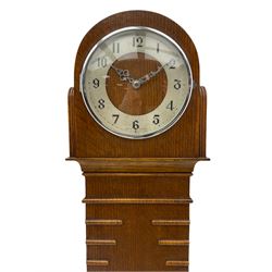 A mid-20th century English art-deco Grandmother clock with a mains powered electric movement chiming the hours and quarters on gong rods, in an oak case with an arched top, long trunk and short plinth on bracket feet, sliver effect chapter ring with Arabic numerals and silvered serpentine hands, with chime/silent facility.



