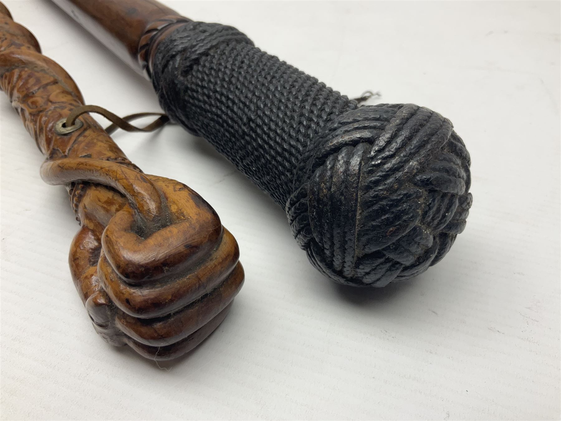 19th century wooden walking stick, the handle carved as a snake within a clenched fist, the cane carved with foliate and cross hatched decoration, with a metal spike to base, together with a turned wooden walking stick, with lacquered rope nautical knot handle, tallest L96.5cm