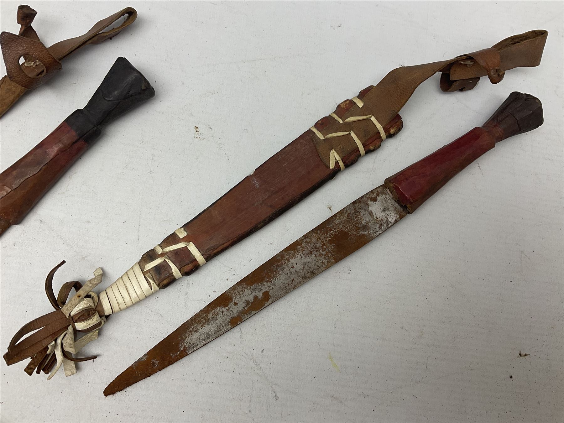 Indian kukri with 29cm curving steel blade and nickel mounted horn grip; in leather covered scabbard with one skinning knife L42cm overall; Hitler Youth knife with scabbard in relic condition; and three African graduated knives each with crudely carved wooden grips and painted leather covered scabbards (5)