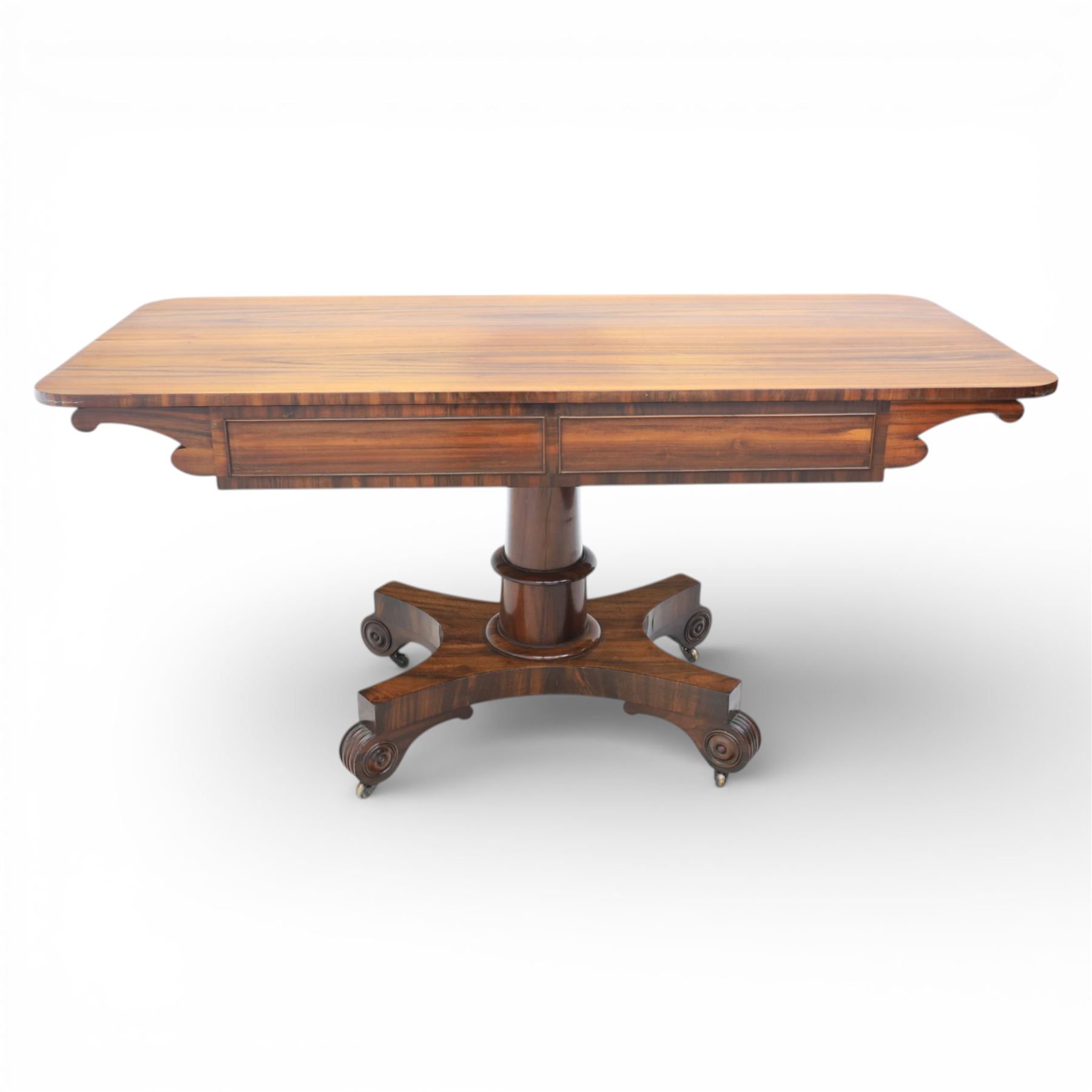 Victorian rosewood library table, rounded rectangular top with two frieze drawers with turned wooden knobs, quatriform base with scrolled ends terminating in brass castors  