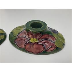 Pair of Moorcroft candlestick holders in Clematis pattern, together with Moorcroft ashtray and vase of squat baluster form, both in Hibiscus pattern, all with paper label and impressed marks beneath