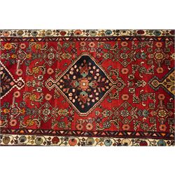 Large Persian Qashqai runner rug, the red ground decorated with navy and ivory lozenge medallions interspersed with stylised floral and geometric motifs, enclosed by an ivory flowerhead border and patterned guard stripes