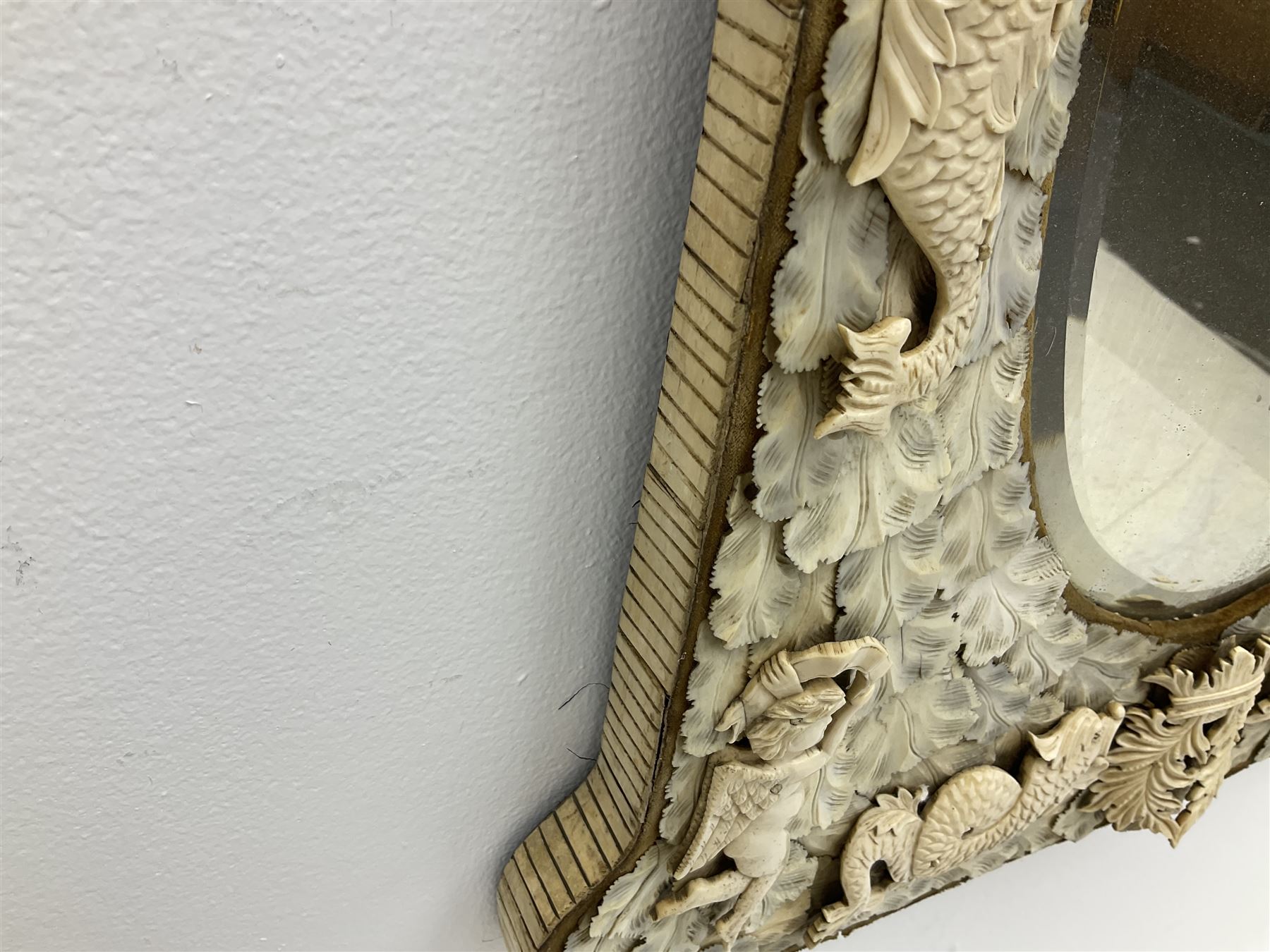 Pair 19th century French Dieppe bone and ivory wall mirrors, the oval bevelled mirror plates within rectangular frames with shaped tops, profusely decorated with ivory leaves, further detailed with carved bone armorial type crest inscribed 'SGOTORVM', putti, fish and mask heads, H81cm W48cm