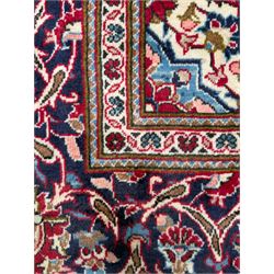 Central Persian Kashan hand-knotted carpet, the deep red ground with a central lozenge medallion in ivory and navy, surrounded by dense scrolling floral and vine motifs, navy spandrels and a wide border with stylised palmettes and flowerheads enclosed by multiple guard stripes