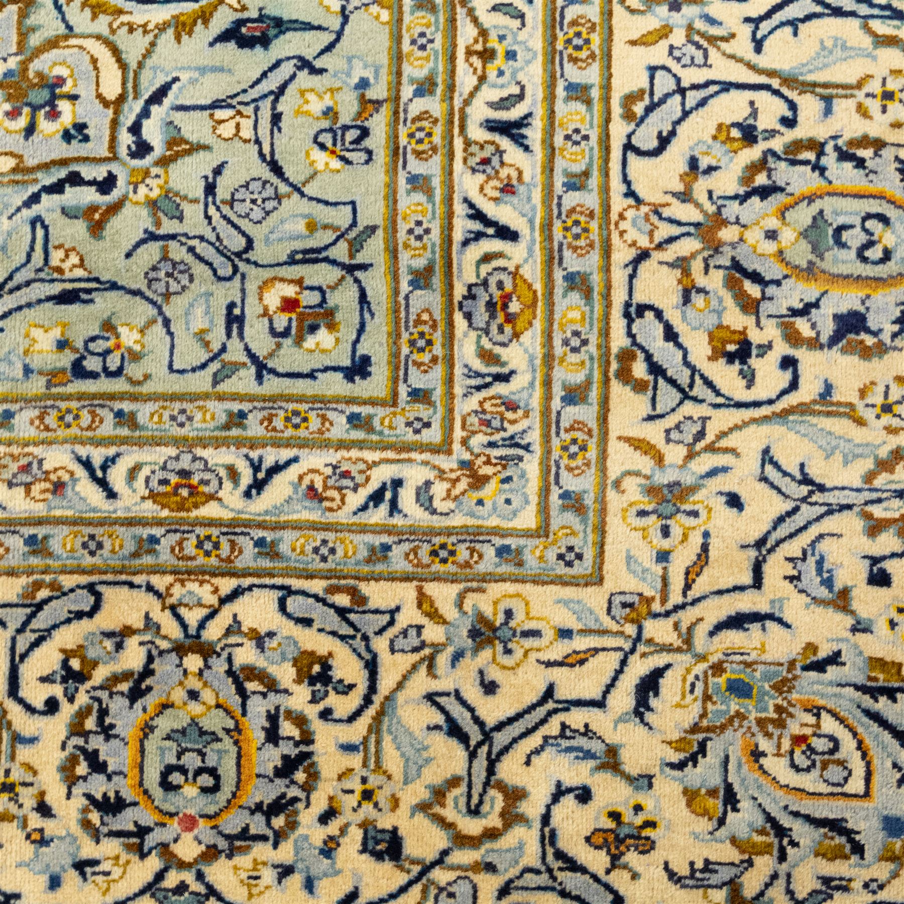Central Persian Kashan hand-knotted carpet, pale celadon blue ground, decorated with an all-over central floral and foliate design with rosette medallion incorporating scrolling vine work, palmettes, and stylized blossoms  highlighted in tones of indigo, ivory, gold, and powder blue, enclosed by a cream ground border, flanked by multiple guard stripes, with cotton fringe ends 