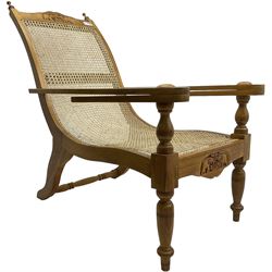 Late 20th century teak framed plantation chair, cresting rail and apron carved with two elephants with upraised trunks, flanked by finials, cane back and seat, fitted with hinged extending leg rests, on ring turned supports