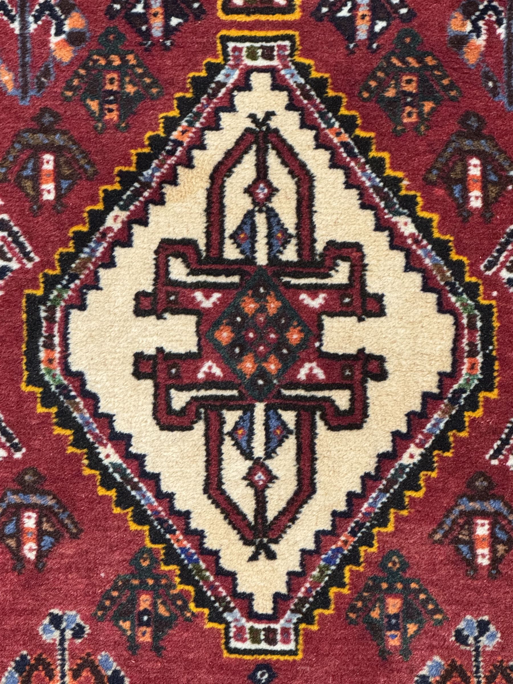 Persian Qashqai crimson ground runner, the field decorated with repeating diamond-shaped medallions flanked by angular floral motifs, the spandrels with intricate boteh designs, framed by an ivory border with stylised floral patterns and scrolling vines