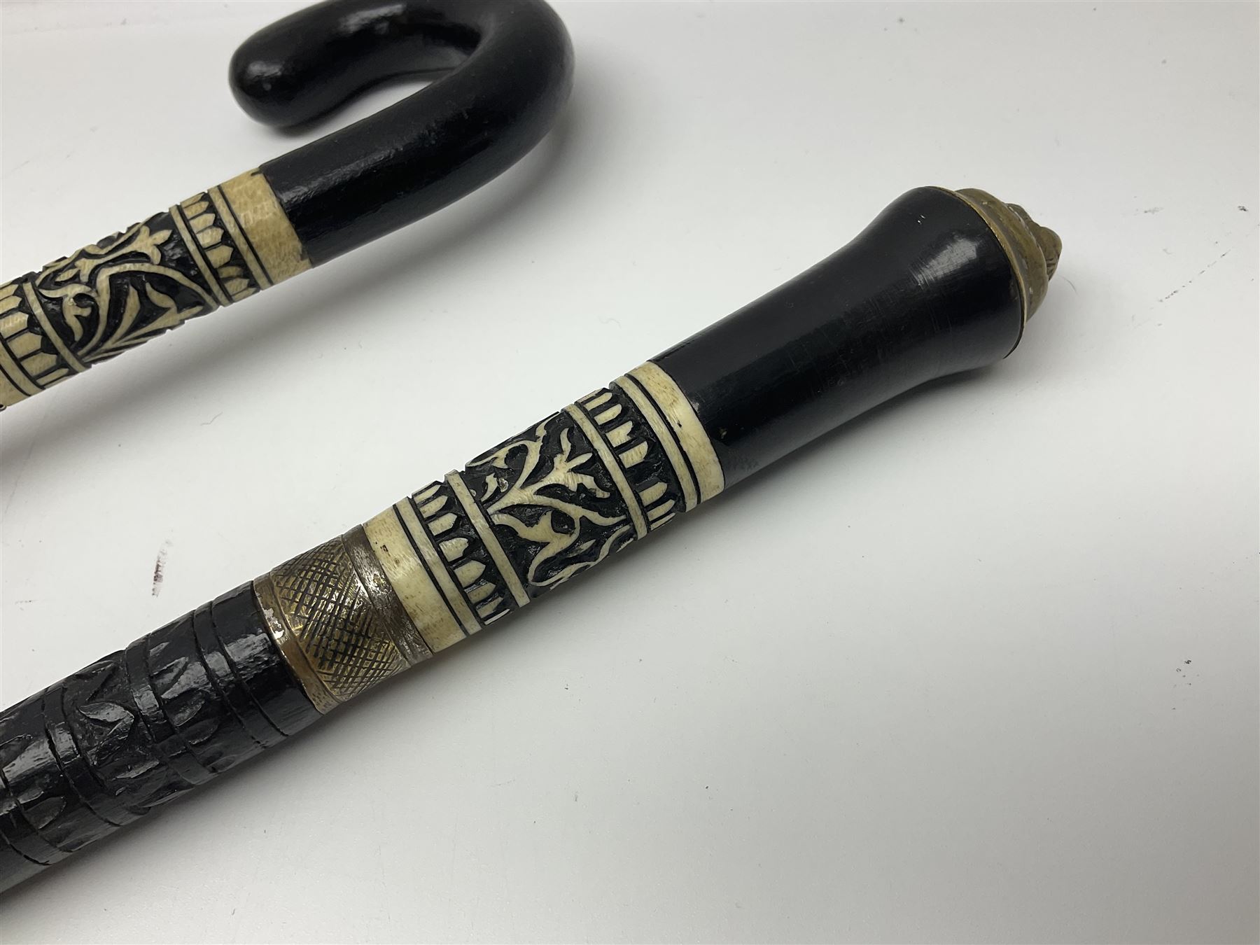 Early 20th century Indian ebonised wooden umbrella sword stick with 36cm blade, carved bone mount and black cloth cover L92cm overall; together with a similar Indian ebonised wooden sword stick with 64cm blade, carved bone mount and brass lion mask pommel L91cm (2)