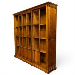 Wesley Barrel - large cherry wood bookcase, with projecting cornice and fielded panelled sides, with three sections comprising three fixed shelves, sliding glazed and panelled doors, moulded plinth base