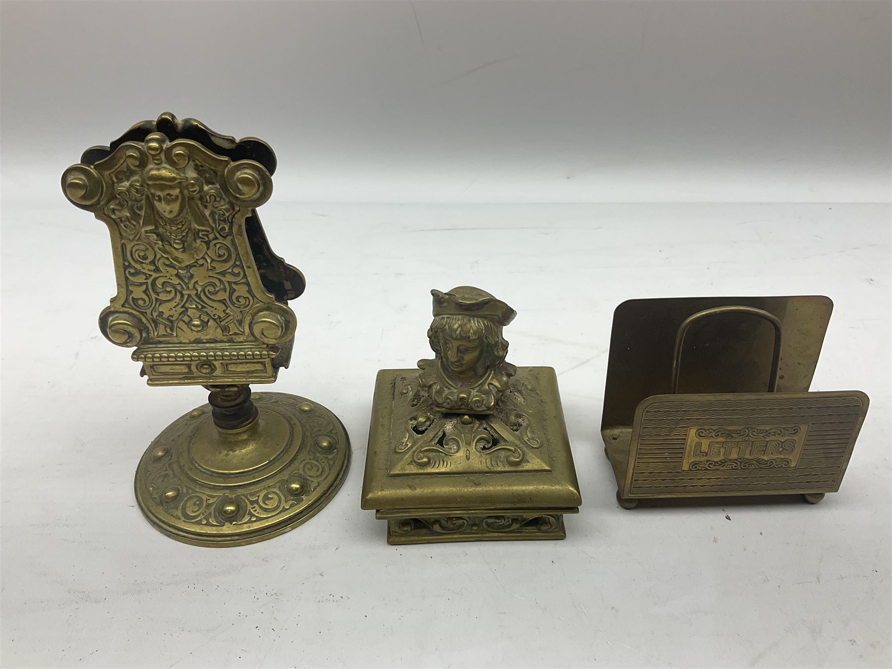 Collection of victorian and later brass desk accessories, to include a letter holder with cherub design, ink well of square form with hinged lid, brass table bell, brass casket with relief decoration, etc  