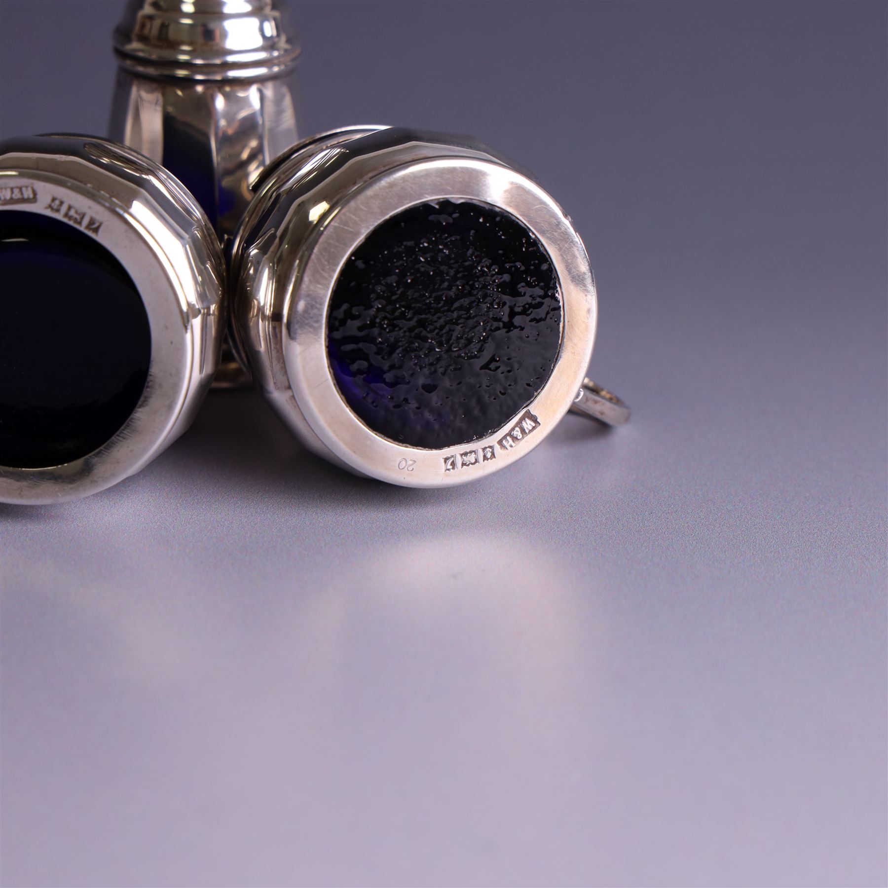 Mid 20th century three piece silver cruet set, comprising pepper shaker, open salt and mustard pot with cover, each of circular faceted form, hallmarked Walker & Hall, Birmingham 1958, the mustard pot and salt with blue glass liners