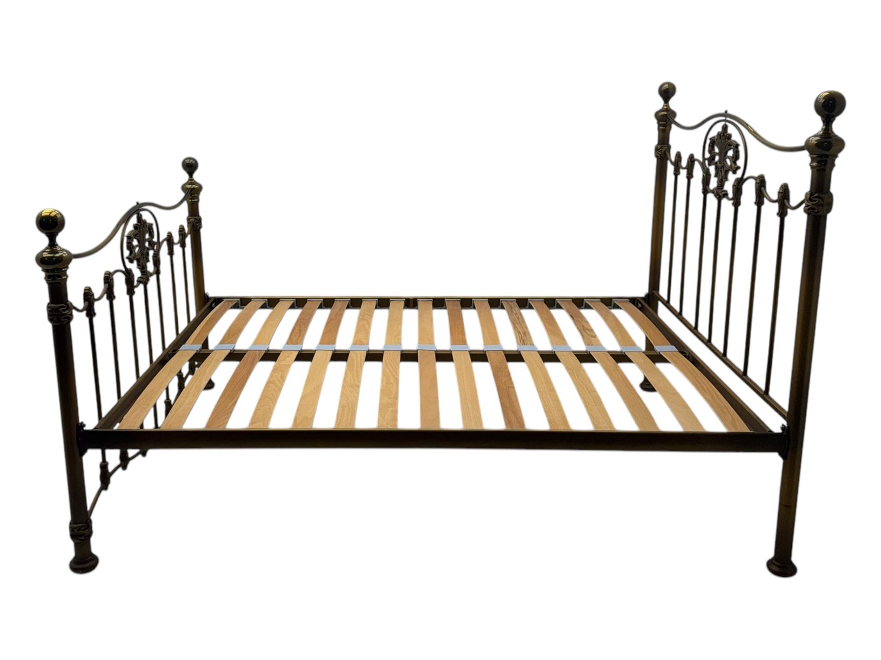 Victorian design king size brass bed frame, featuring an arched headboard and footboard with intricate cast floral and scrollwork centre motifs, flanked by cylindrical supports with ball finials and decorative collars, raised on rounded feet, with a slatted wooden base