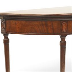 Georgian mahogany demi-lune card table, the lunette shaped top with cross-banded and boxwood-strung edge, opening to reveal baize-lined interior and supported by rear gatelegs, over a banded frieze with applied oval plaques, raised on turned and tapering supports