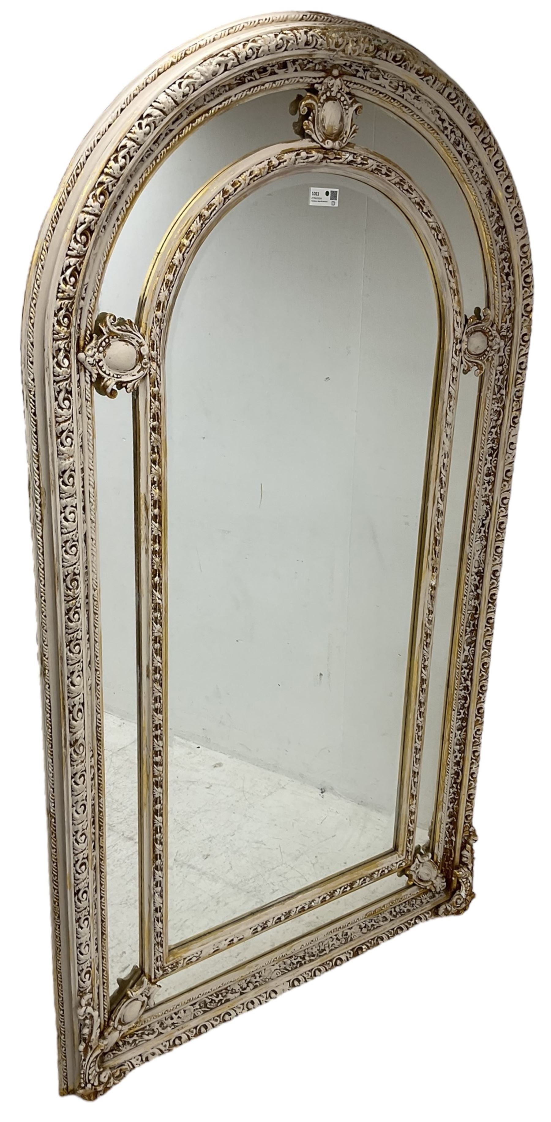 Large painted and gilt arched wall mirror, the frame decorated with scrolling leafy branches, central bevelled mirror mirror surrounded by plain panels, decorated with cartouche mounts 