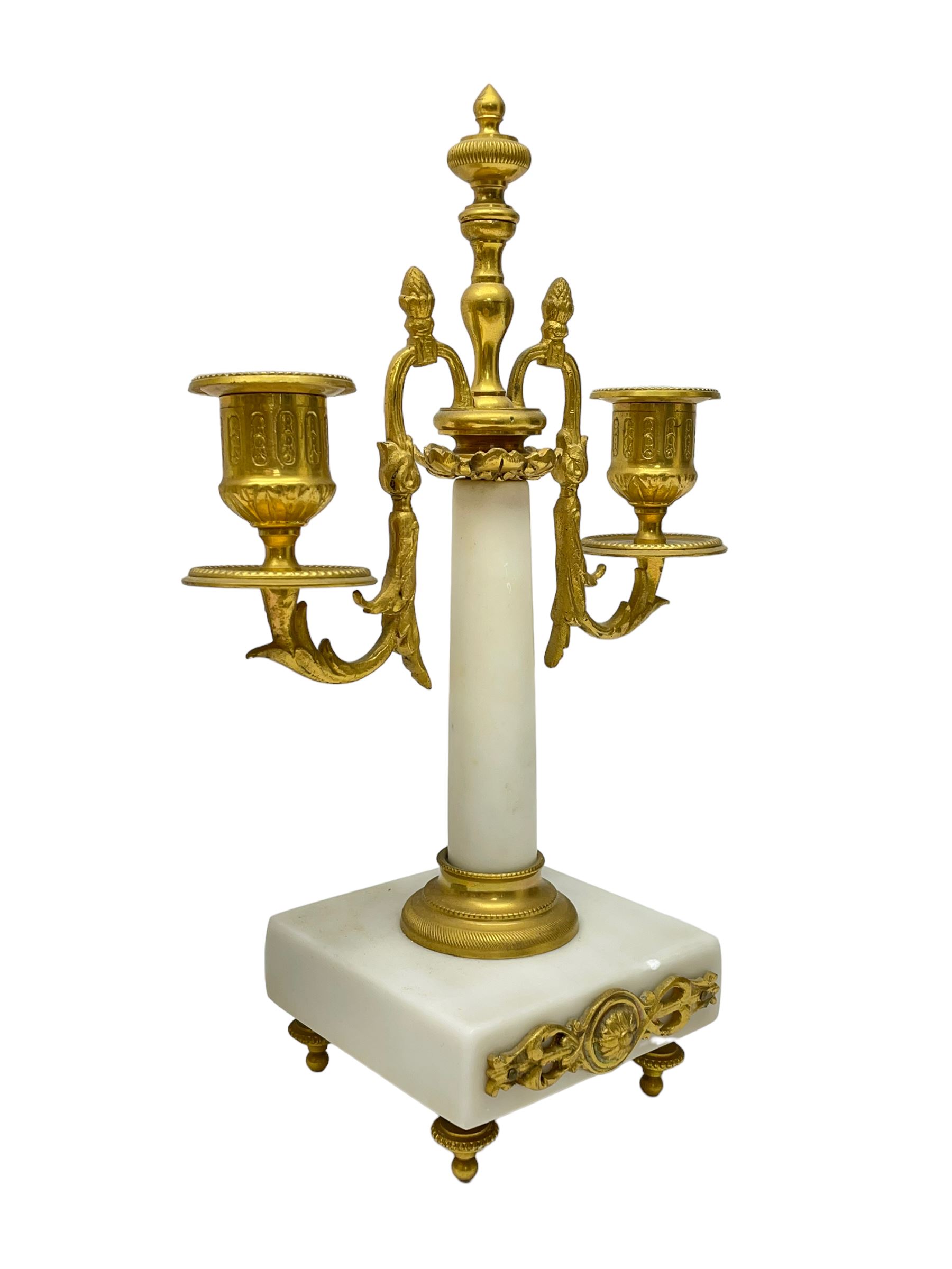 French - Late 19th century 8-day white marble and gilt metal portico clock garniture, the clock surmounted by an urn and raised on a pair of cylindrical pillars above a rectangular plinth base, white enamel dial with Arabic numerals and floral garlands, twin train countwheel striking movement, striking the hours and half hours on a bell, with a sunburst pendulum and gilt Louis XVI hands, garniture with matching twin light candelabra. With Key.   Candelabra H 30cm.