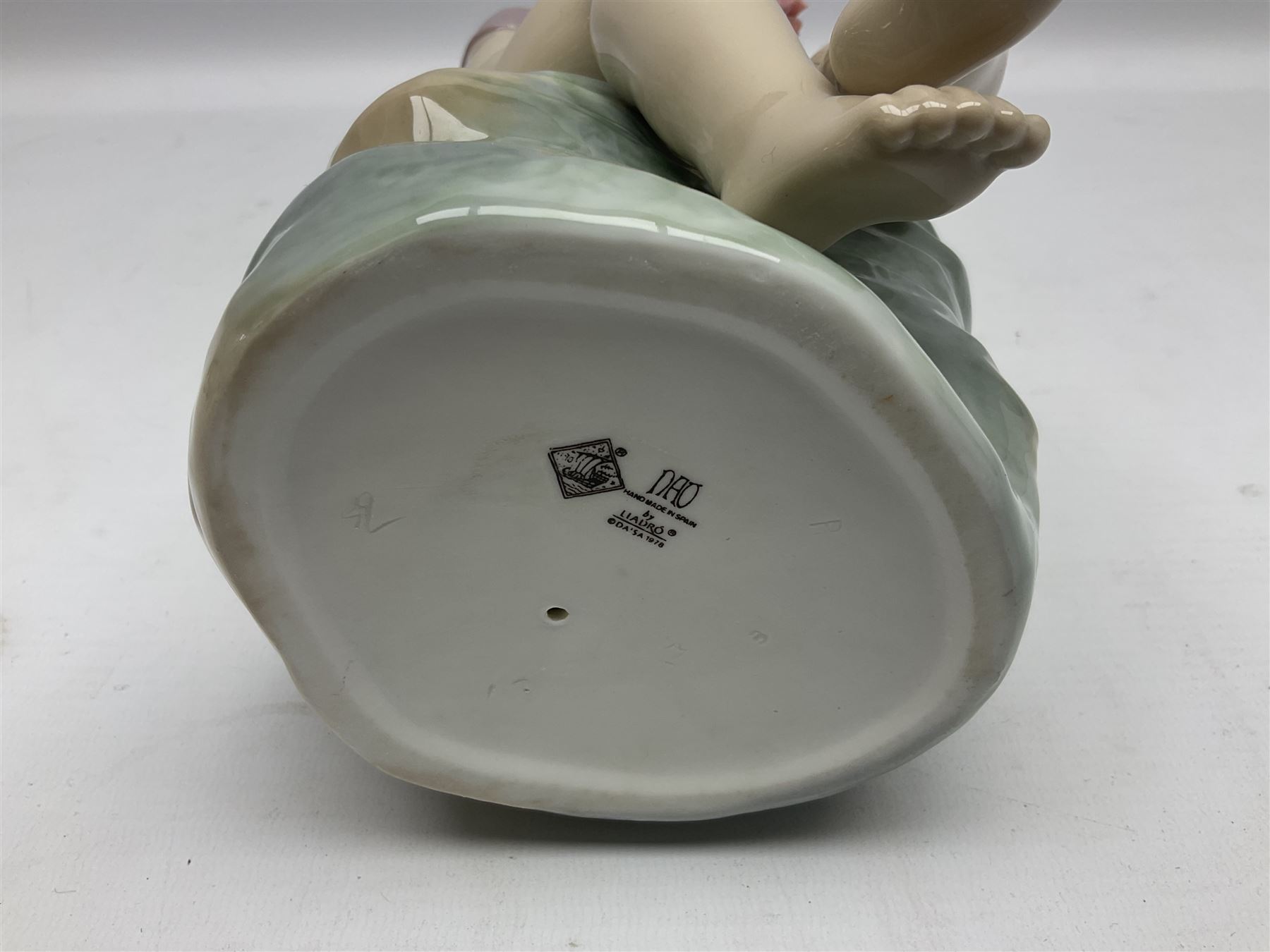 Large Nao figure modelled as a young girl seated upon a rock holding a rose, H30cm