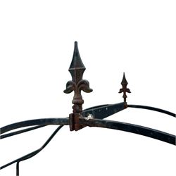 Antique wrought iron strapwork garden arch, with scroll form arched top with spearhead finials, over integral side trellis panels, in distressed black-painted finish