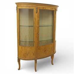 Edwardian satin walnut display cabinet, bowed oval form with moulded and dentil cornice over glazed panels, enclosing a laurel wreath damask interior with adjustable glass shelves, the frame applied with gilt metal bead mouldings and mask mounts, enclosing a shelved interior, raised on cabriole supports with moulded feet