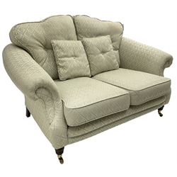 Lincoln House - two-seat sofa, shaped frame with rolled arms, upholstered in pale blue fabric with repeating foliage pattern, on turned front feet with brass cups and castors 