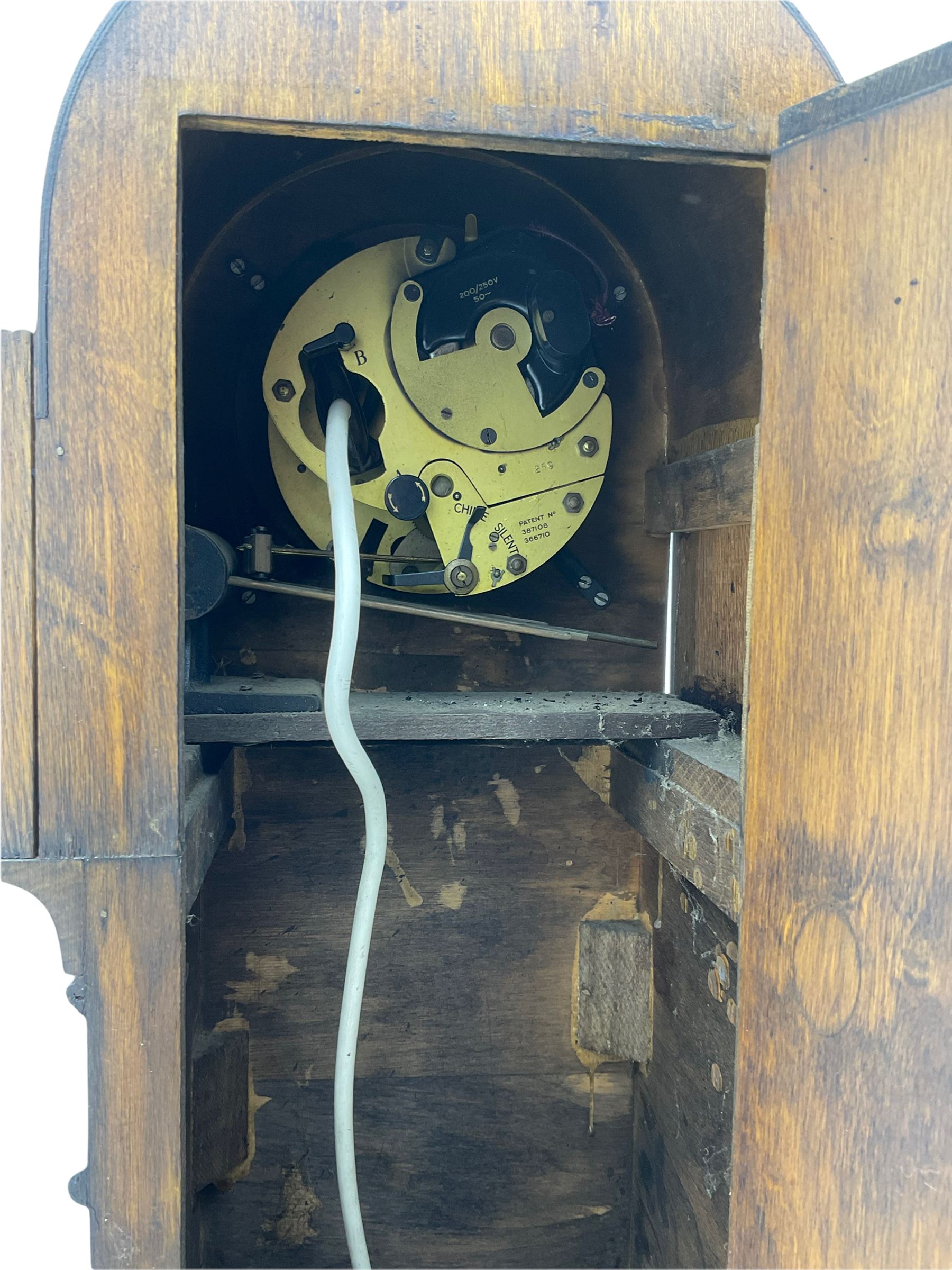 A mid-20th century English art-deco Grandmother clock with a mains powered electric movement chiming the hours and quarters on gong rods, in an oak case with an arched top, long trunk and short plinth on bracket feet, sliver effect chapter ring with Arabic numerals and silvered serpentine hands, with chime/silent facility.



