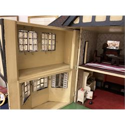 Large Tri-ang No.93 doll`s house in the 'Stockbroker's Range' c1935; two-storey double-fronted Tudor design, half timbered gables, two-storey bay windows, cream and mock shrubbery to front, opening metal framed windows with green shutters, red simulated tiled roof with chimney, integral garage with opening doors, front elevation has four hinged doors opening to reveal two bedrooms with fire places, living room, bathroom and kitchen with built in dresser and sink, entrance hall and staircase, side entrance with porch and seat and sun dial over on chimney stack; some wiring for electrical lighting; metal Tri-ang Toys disc verso; comprehensively furnished H66cm L117cm D43cm
