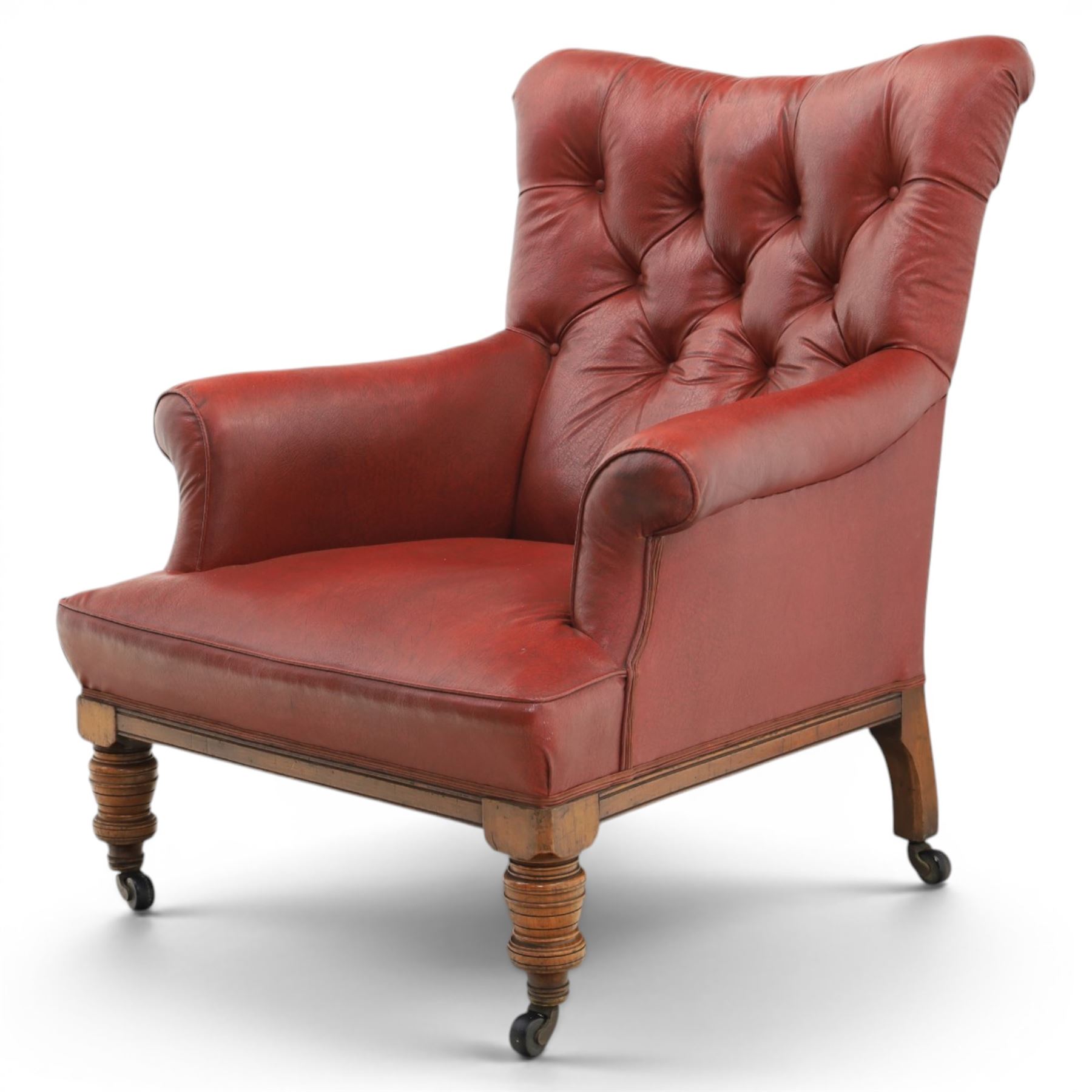 Early 20th century style oxblood red leather Chesterfield armchair, deep buttoned shaped back over padded scroll arms and loose seat cushion, raised on turned mahogany front supports with brass caps and castors
