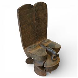 African carved hardwood ceremonial seat, monoxylous construction with twin dished seat wells, the tall back incised with repeating geometric triangular motifs, the front carved in the form of a tribal mask with projecting features, raised on a cylindrical base with ribbed and textured carving