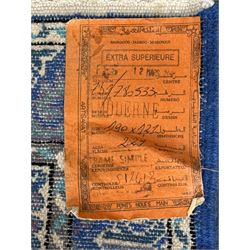 Morrocan single weft blue ground rug, the field segmented into a grid of ten rectangular panels, bordered by a series of guard bands with repeating floral and geometric patterns with interlocking vines and rosettes, the edges finished with a fringe of twisted tassles