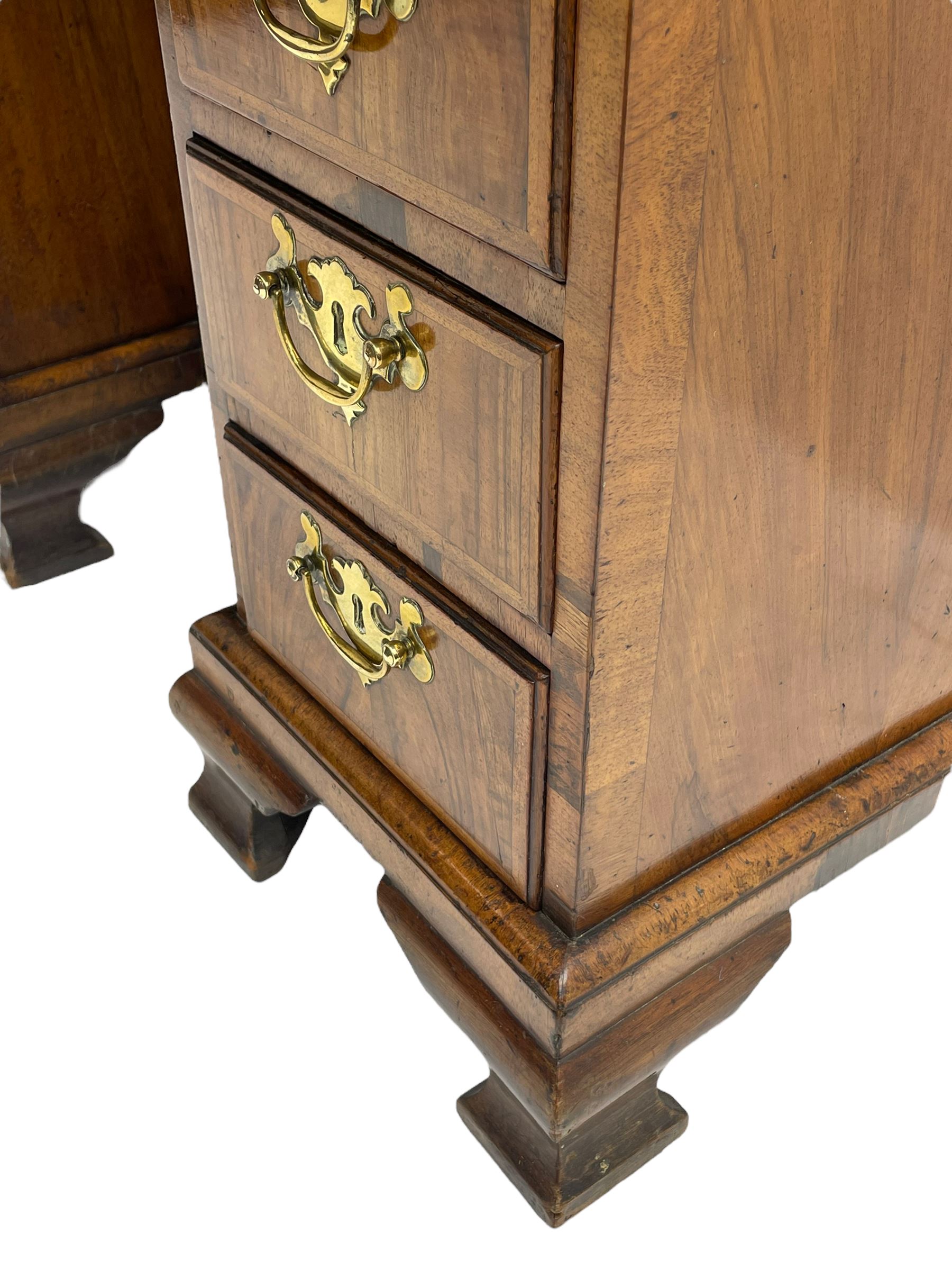 Early 18th century Queen Anne figured walnut kneehole desk with secretaire drawer, moulded and book matched top with walnut band, the top drawer with fall front enclosing small drawers and pigeon holes, fitted with nine drawers and central recessed cupboard, on ogee bracket feet