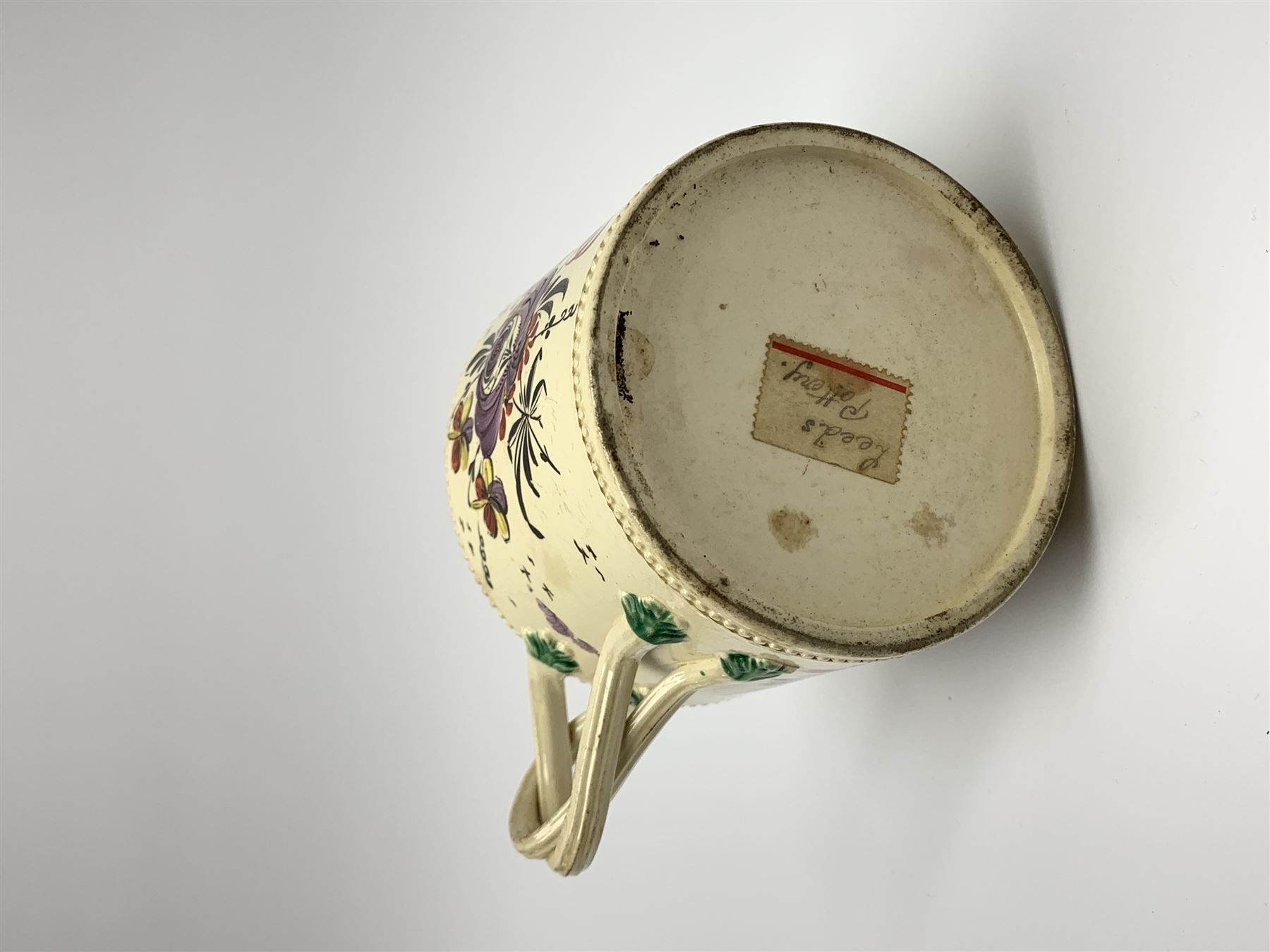 18th century creamware teapot, probably Leeds, with reeded entwined handle and floral finial to the cover, the body with hand painted polychrome decoration of figure to one side, and floral spray to the other, collectors paper label beneath inscribed Leeds Pottery, H11.5cm