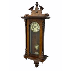 Eight-day early 20th century rack striking German spring driven Vienna wall clock striking on a coiled gong, deadbeat escapement with adjustable steel pallets, two-piece enamel dial with roman numerals and minute track with half-hour markers, spun brass bezel, decorative steel Viennese hands, gridiron pendulum inscribed R/A, mahogany and ebonised case with a glazed full length arched door, broken arch pediment with centre finial, veneered concave pendant with finials. With key and Pendulum.