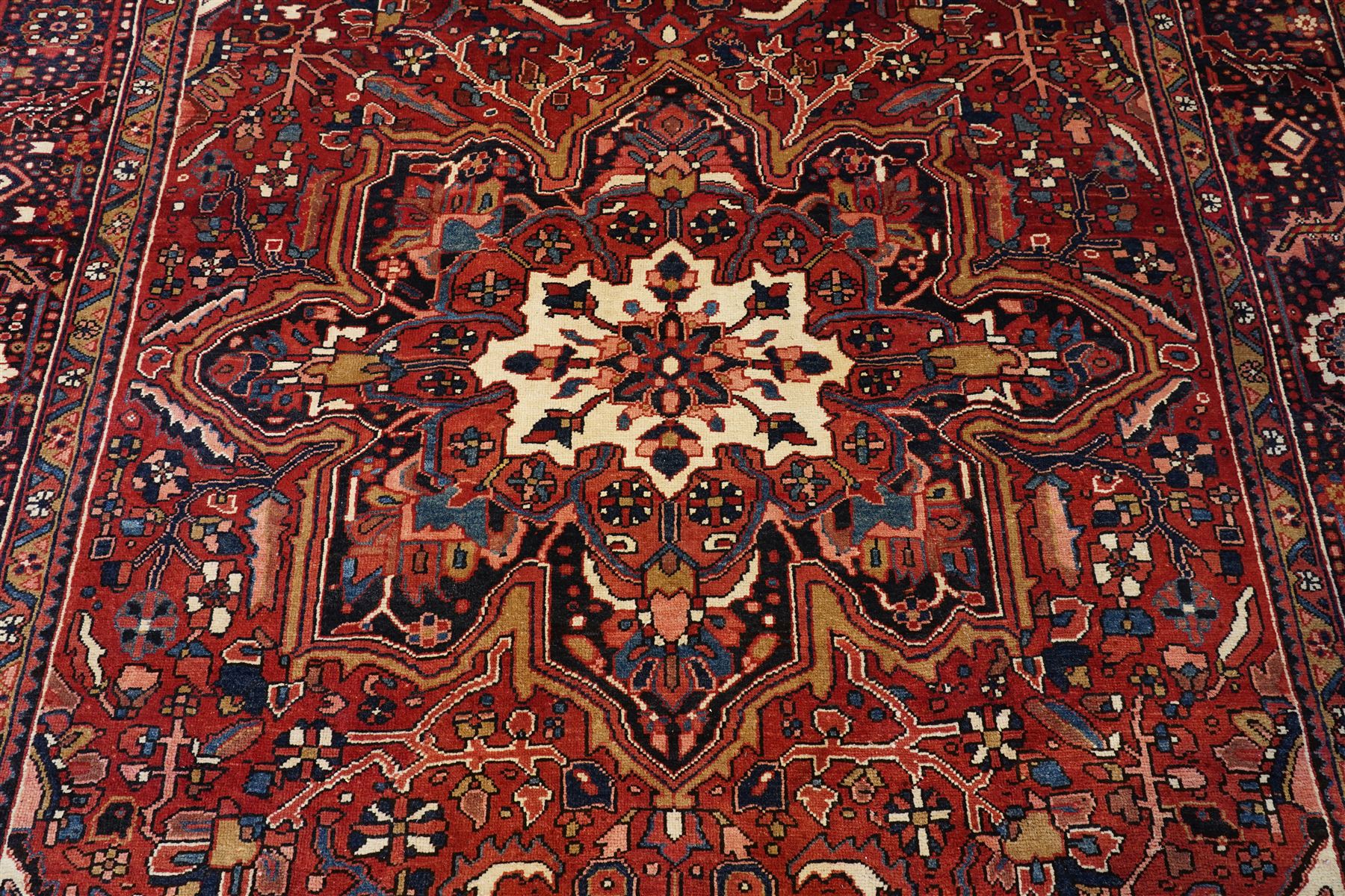 North West Persian Heriz/Ahar hand-knotted carpet, brick red field with a central bold stepped star medallion with pendants, surrounded by angular floral and geometric motifs, ivory spandrels, enclosed by a dark indigo border of stylized rosettes and vine motifs with multiple guard stripes, cotton fringe ends 