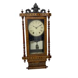 A late 19th century spring driven American Eight-day wall clock, striking the hours on a bell, in a parquetry case with contrasting oak, maple, walnut, and other hardwoods, with a flat top, carved cresting and finials rectangular glazed door flanked by finely turned pilasters, with a painted dial with roman numerals and minute track, steel spade hands and faux mercury pendulum reflected in a rear case mirror.   


