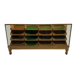 Early 20th century oak framed haberdashery shop counter, glass panel exterior enclosing sixteen graduating drawers with oak fronts and handles, raised on shaped tapering supports 