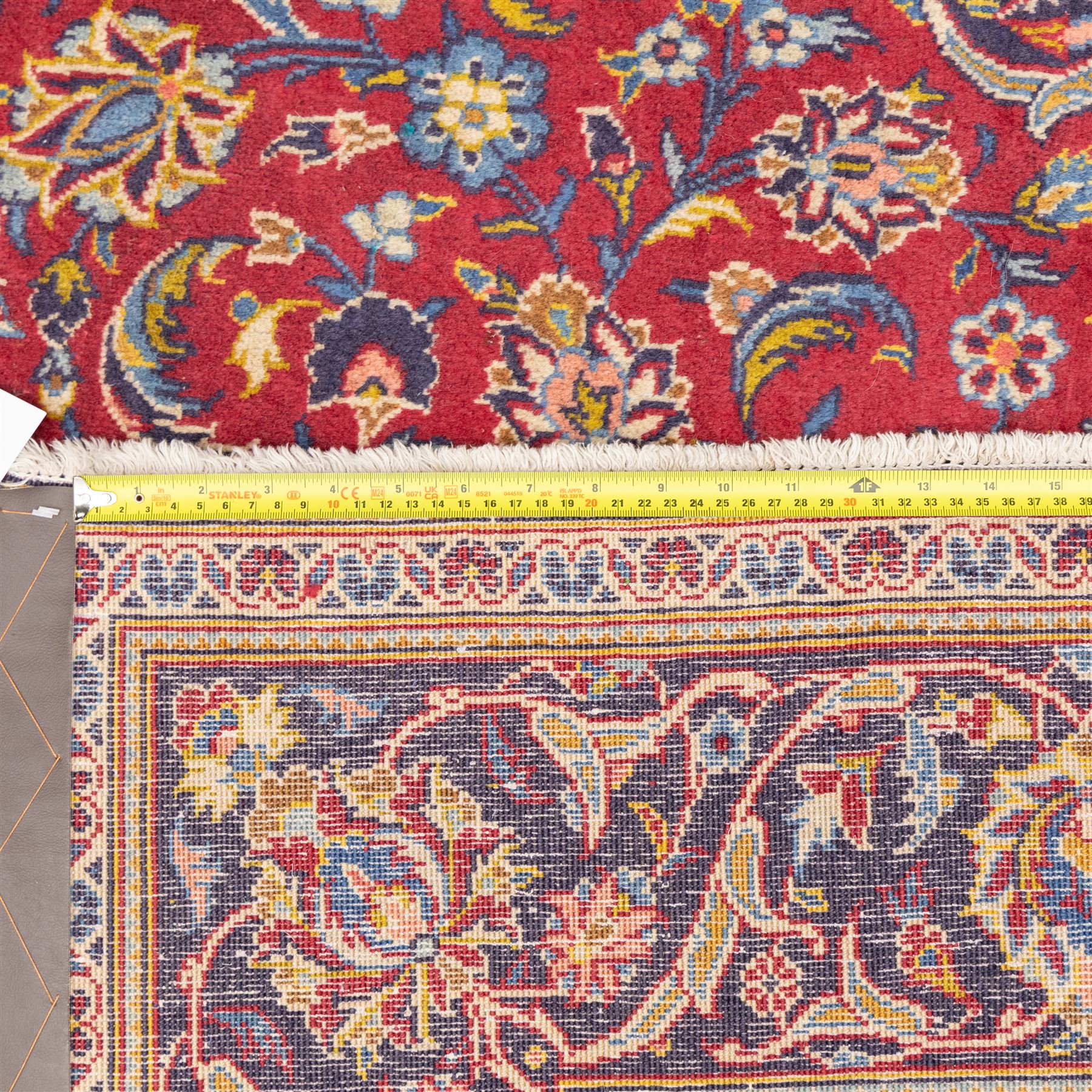 Central Persian Kashan hand-knotted rug, crimson field, profusely decorated with scrolling vines and palmettes, floral sprays around an ivory and indigo lobbed medallion enclosed by spandrels within an indigo border of arabesques between multiple guard stripes  