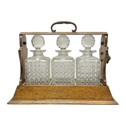 Edwardian oak tantalus, with copper handle, containing with three square cut glass decanters, H32.5cm