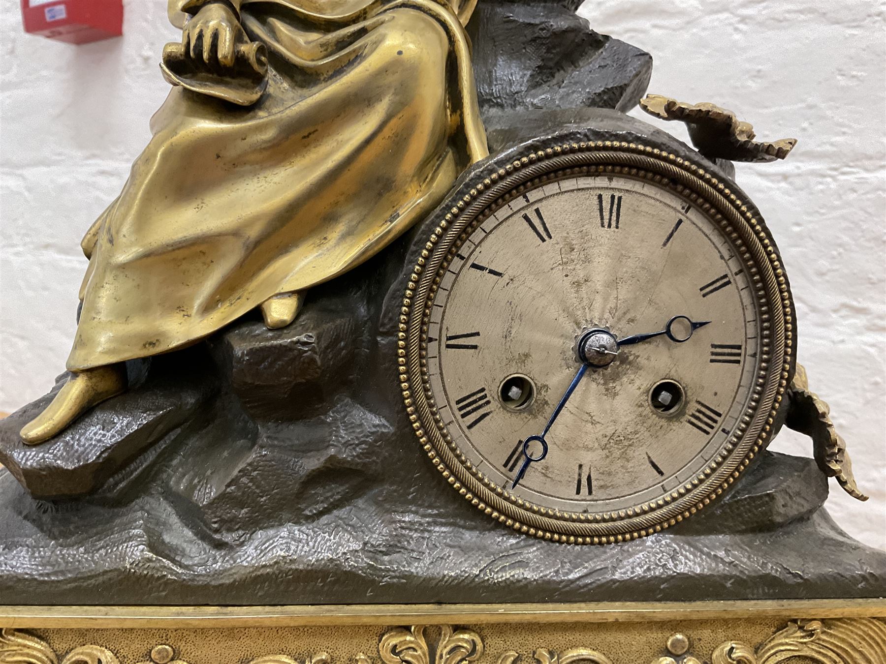 French-Louis XVIII  8-day mantle clock c1820, on a rectangular gilt metal base incorporating repeating cast leaf decoration on a pierced apron and bracket feet, surmounted with a cast brass figure depicting a reclining lady in 18th century dress, Parisian drum movement with a silk suspension and unglazed silvered dial, with Roman numerals and steel moon hands, dial pinned to a countwheel striking movement, sounding the hours and half-hours on a bell. With pendulum and key.
