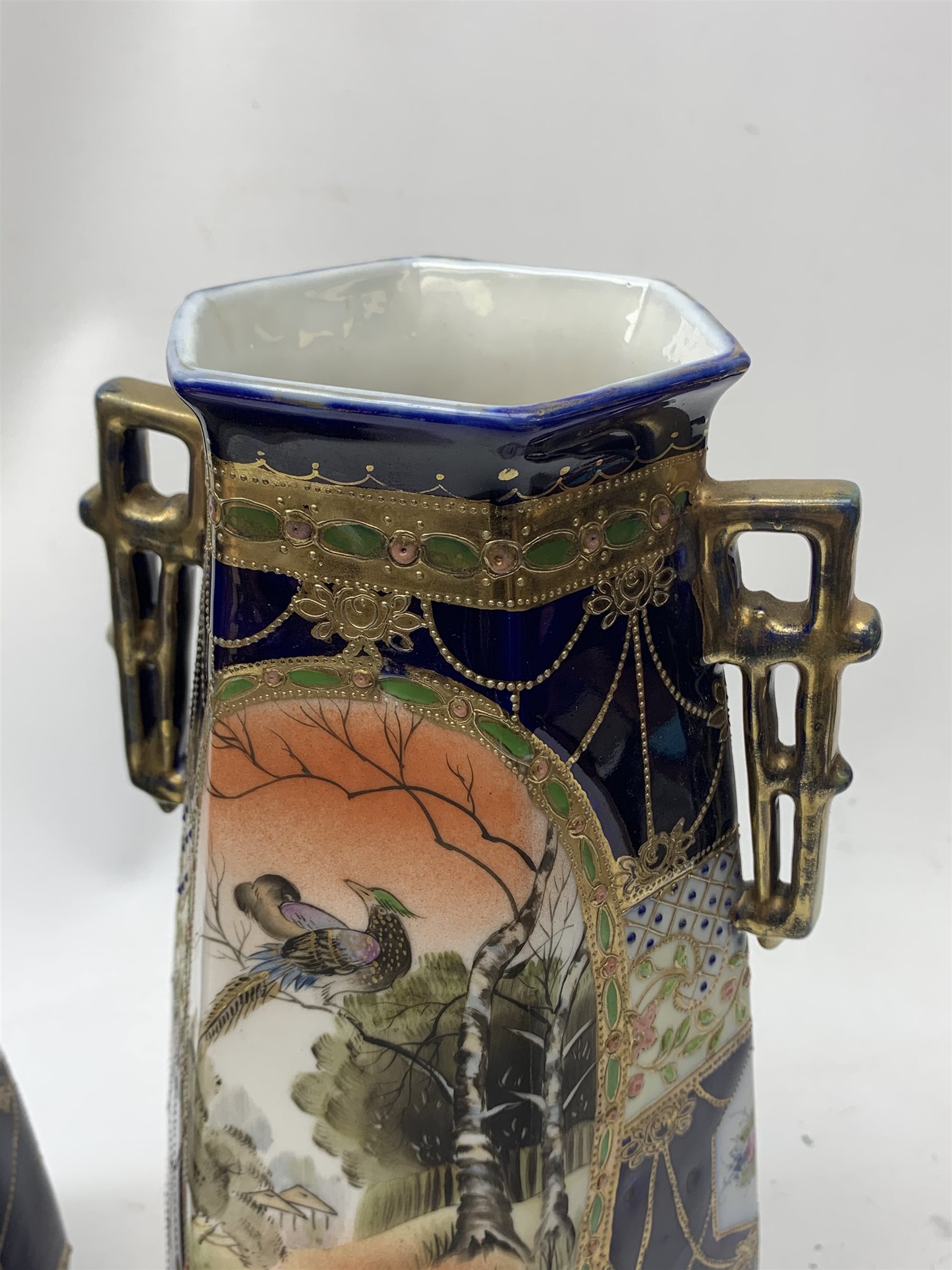 A pair of Japanese Nippon Kinjo vases, of tapering hexagonal form with twin stylised handles, the cobalt blue ground with oval hand painted panels to front and verso depicting landscapes, further detailed with smaller floral bands and panels and heightened with gilt, each with mark beneath, H30.5cm.  