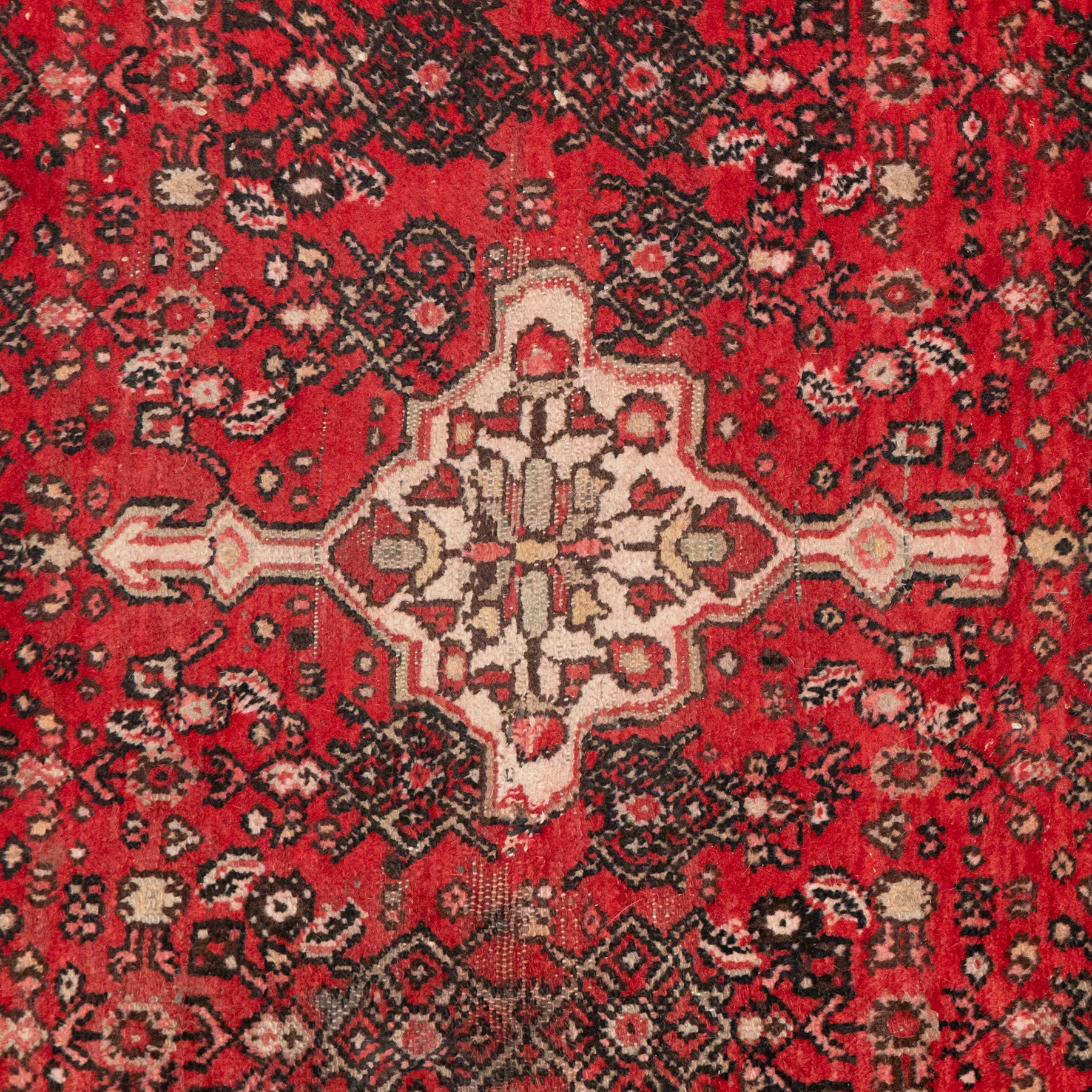 Persian crimson ground runner rug, the field decorated with repeating Herati motifs around an ivory pendant medallion, stepped ivory spandrels with stylised floral ornament, enclosed by a dark ground star border and narrow guard stripes