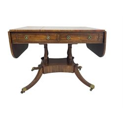 Regency period mahogany drop-leaf sofa table, rectangular top fitted with two cockbeaded drawers with ebony stringing, raised on turned columns united by quadrupod base, the sabre supports terminating in brass cups and castors