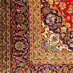 Central Persian Kashan hand-knotted carpet, central field in a ruby red ground with an indigo medallion with pendant motifs, enclosing scrolling arabesques, palmettes, and floral sprays in shades of indigo, turquoise, ivory, and gold, framed by indigo spandrels and a broad floral border between multiple guard stripes 
