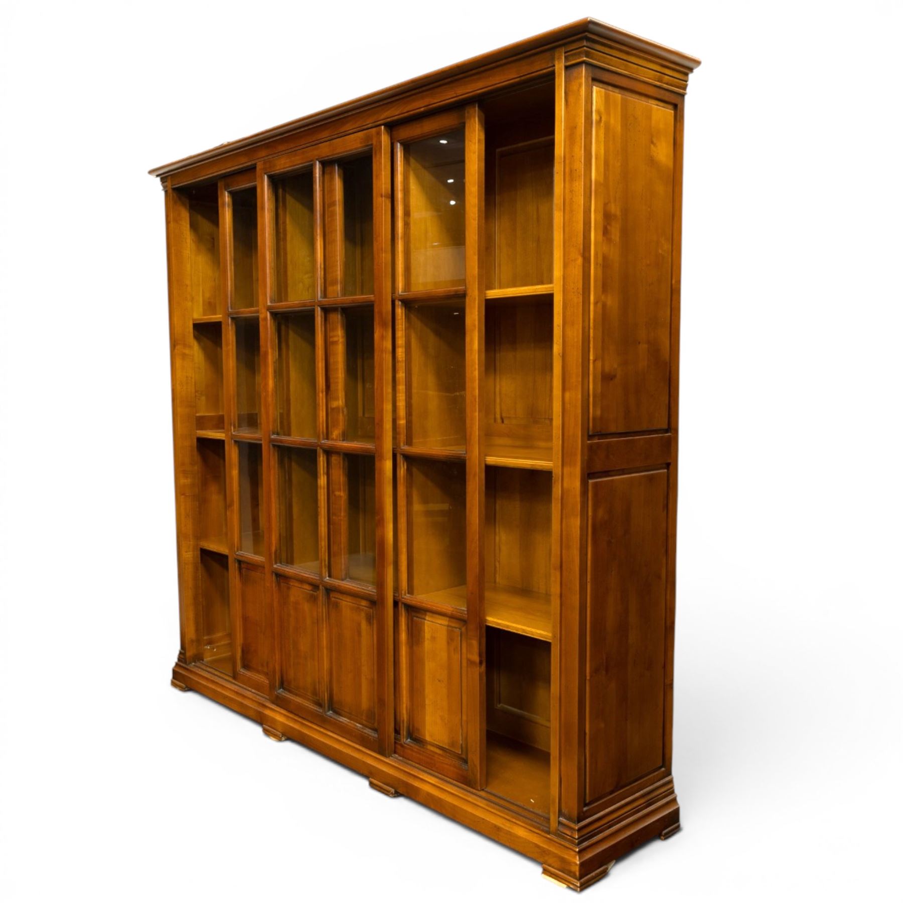 Wesley Barrel - large cherry wood bookcase, with projecting cornice and fielded panelled sides, with three sections comprising three fixed shelves, sliding glazed and panelled doors, moulded plinth base