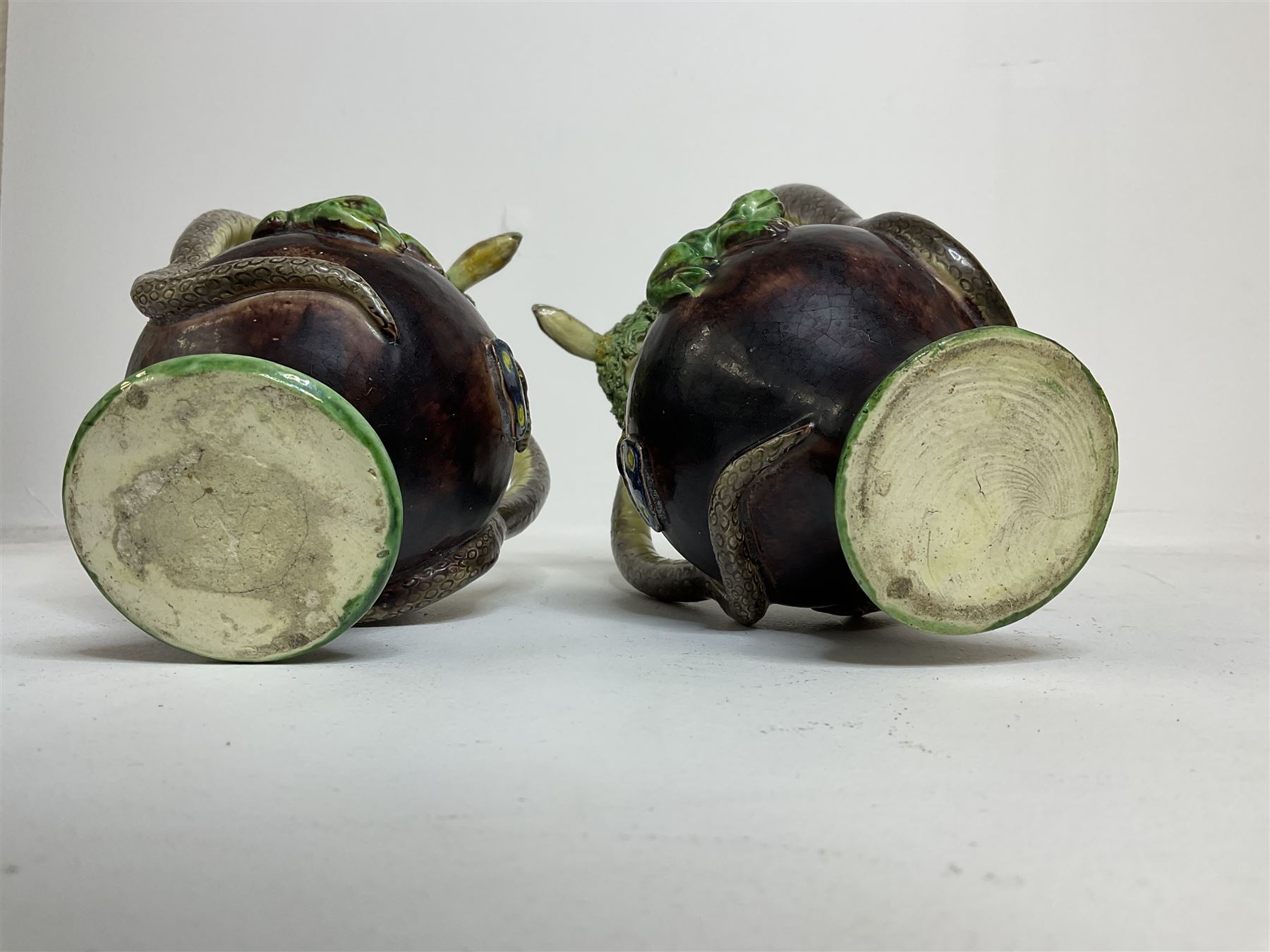 Pair of 19th century Portuguese Palissy style Majolica puzzle jugs, attributed to Manuel Mafra, with mossy rim and pierced lattice neck, twin handles in the form of snakes and the body decorated with frogs, lizards, and moths on a mottled brown glazed ground, unmarked, H20cm