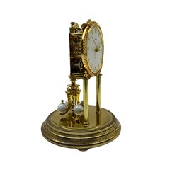 A 20th century Kundo Anniversary 400 Day clock, made by German manufacturer Kieninger & Obergfell, with a gilt brass base and four ball rotary pendulum, white painted dial with gilt three-hour Arabic numerals and batons, with pierced brass hands, open bezel with gilt ropework design, under a glass dome.
No Key. 
