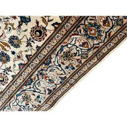 Persian Kashan ivory ground carpet, the field decorated with scrolling branches with foliate and palmette motifs, repeating border with stylised plant motifs, within floral and geometric pattern guard stripes 
