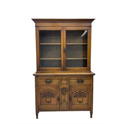 Edwardian walnut bookcase cabinet on cupboard, fitted with two glazed doors above two drawers and two cupboards, the lower cupboard enclosed by two doors carved with tulip motifs
