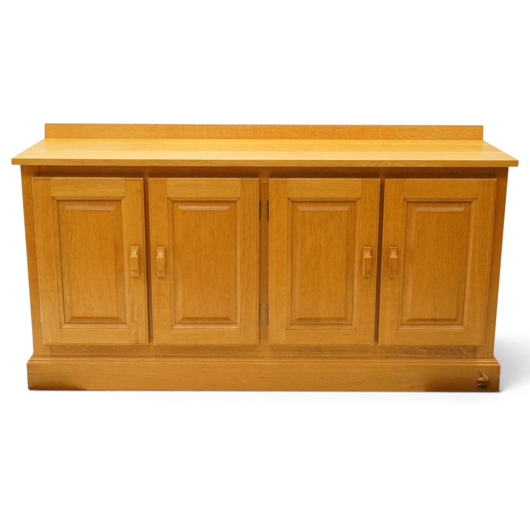 Unicornman - craftsman made oak low-cupboard or sideboard, rectangular top with raised back, fitted with four panelled cupboard doors, on skirted base applied with carved unicorn signature, by Geoff Gell of Coxwold