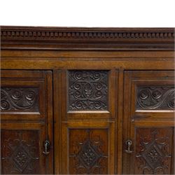 Large 18th century and later oak livery cupboard, projecting moulded and dentil cornice, sunken fillet moulded frame, triple vertical panelled central upright, enclosed by two doors each with five panels, the top row of panels carved with stylised scrolls, the lower panels carved with foliate lozenges, on shaped bracketed skirt base 