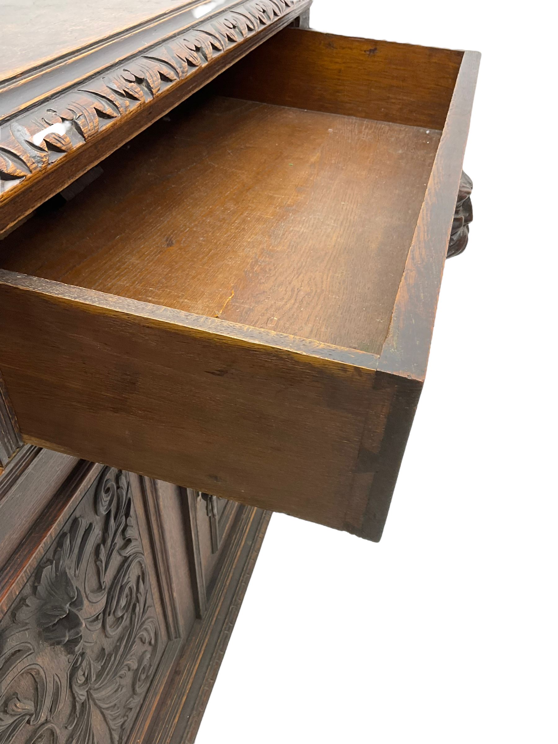 Victorian heavily carved oak sideboard, the moulded top carved with foliate decoration to the edge, fitted with two drawers and three cupboards, the drawer fronts carved with green man mask handles and scrolling foliage, the panelled doors carved with interlacing foliage, on turned compressed bun feet